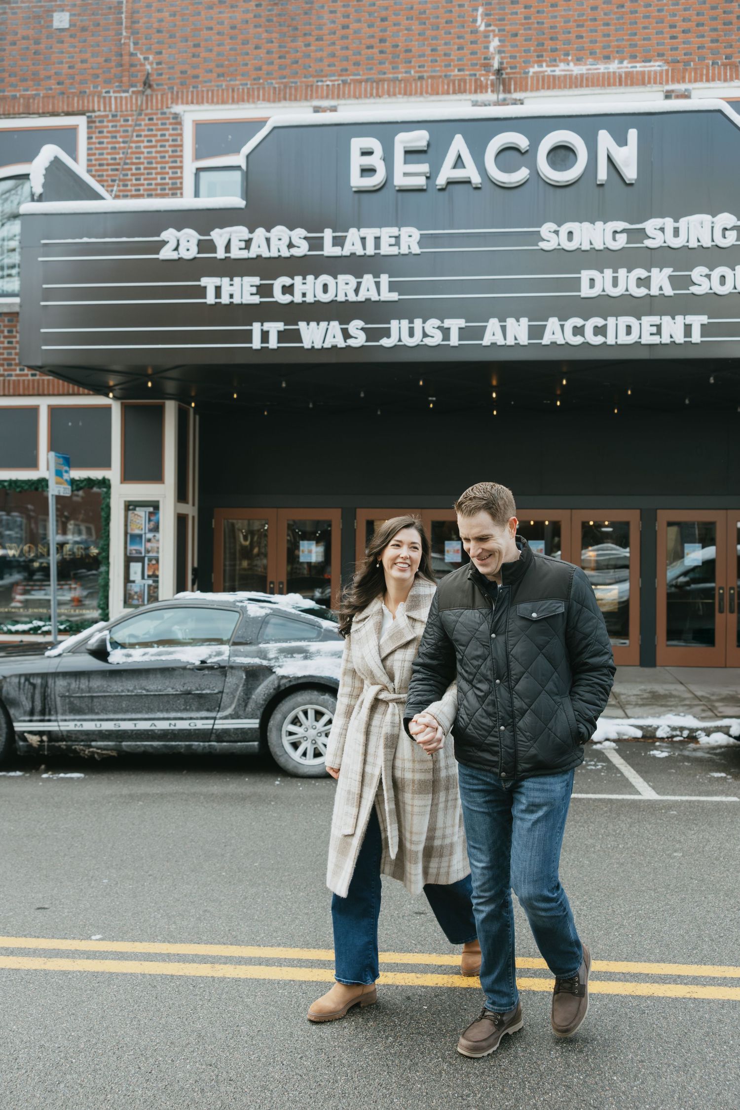 Couple holding hands and smiling in front of the Beacon Theatre marquee on a winter day.