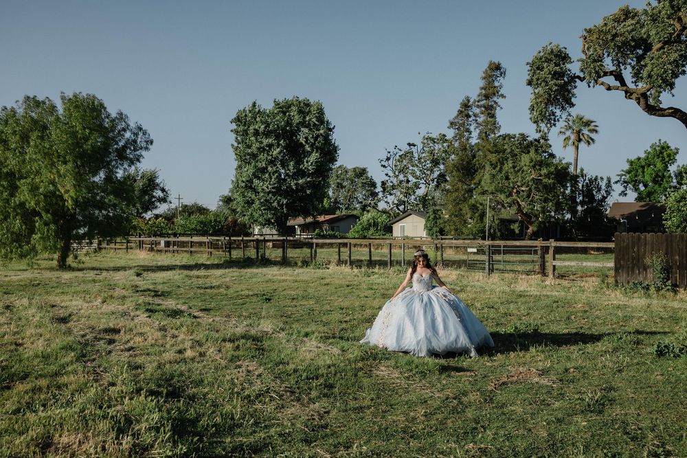 Young girl in a blue ball gown walks through a green farm field on a clear sunny day.