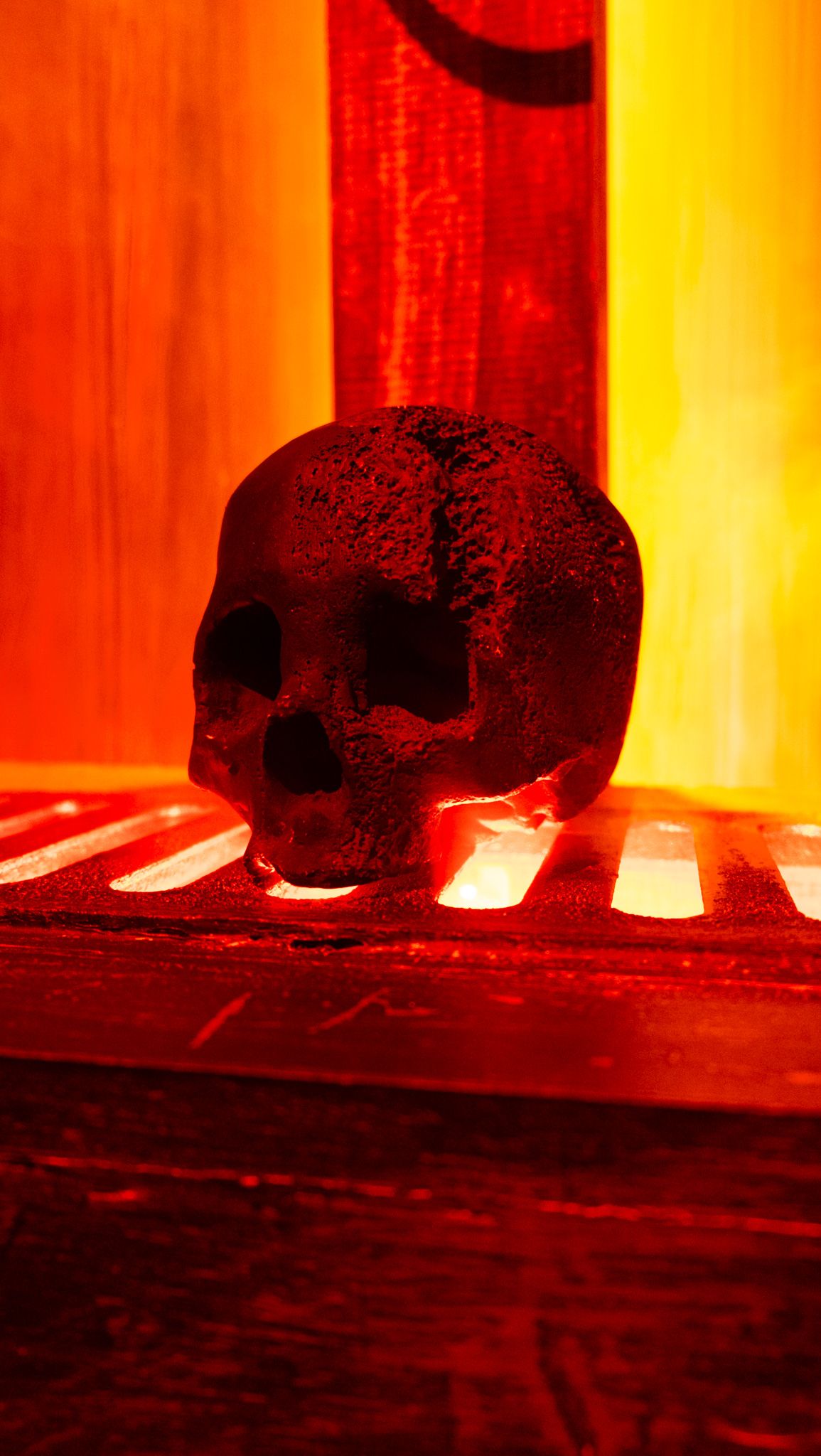 Dark skull figurine glowing with eerie red and orange light, creating a dramatic Halloween or gothic horror atmosphere.