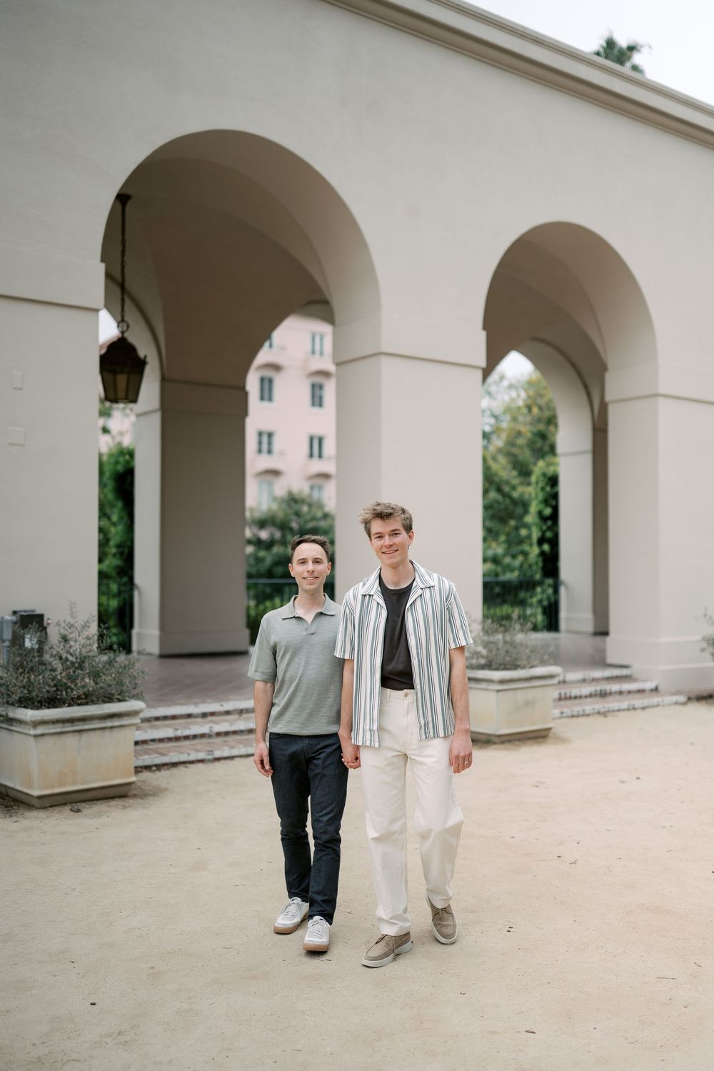 Two young men standing in front of elegant arched colonnade building outdoors on a sunny day.
