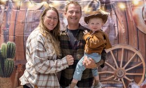 Family of three posing at a western-themed birthday party, parents in flannel shirts holding toddler in cowboy hat.