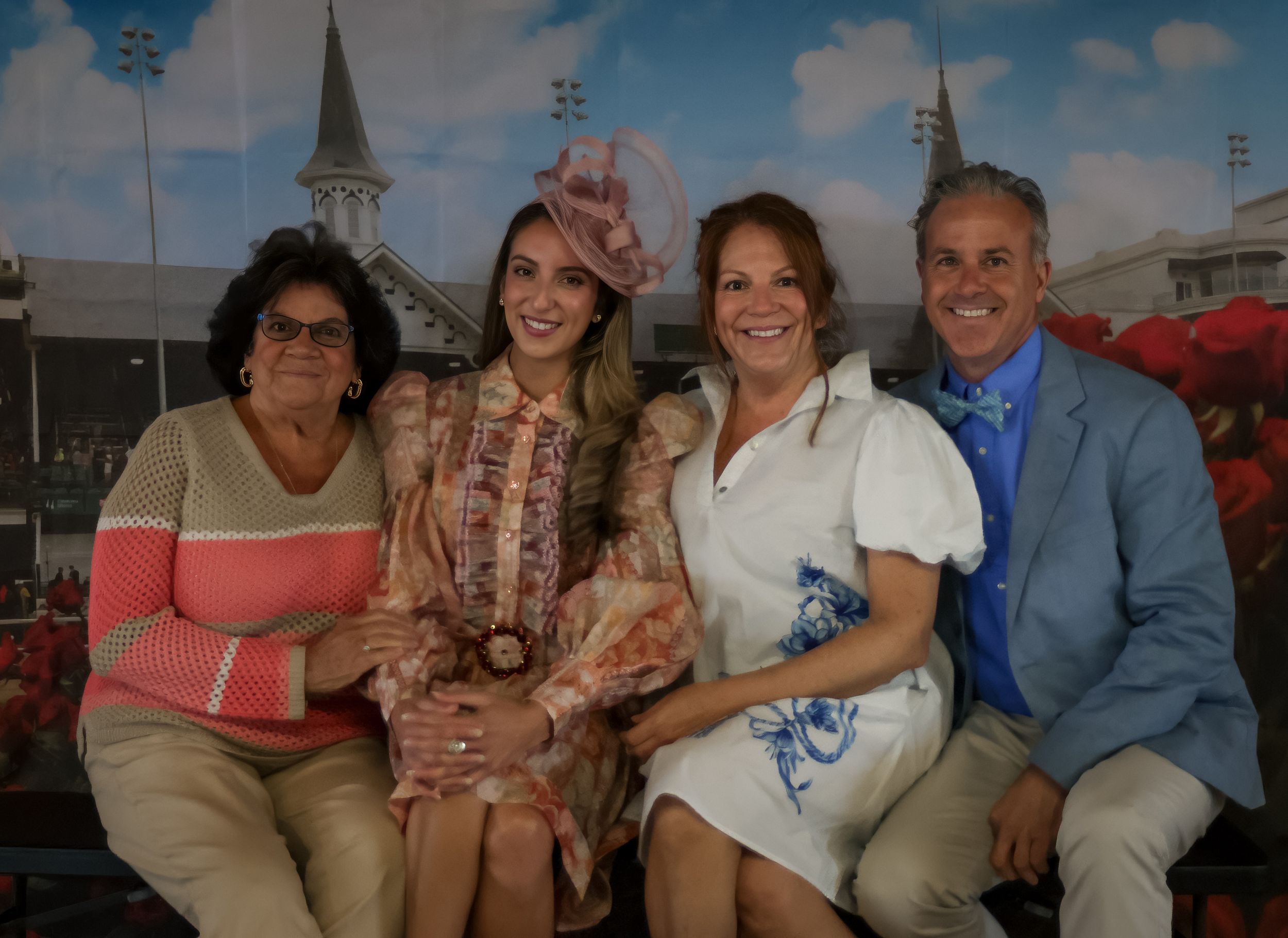 Family of four poses together at Kentucky Derby themed photo backdrop with twin spires.