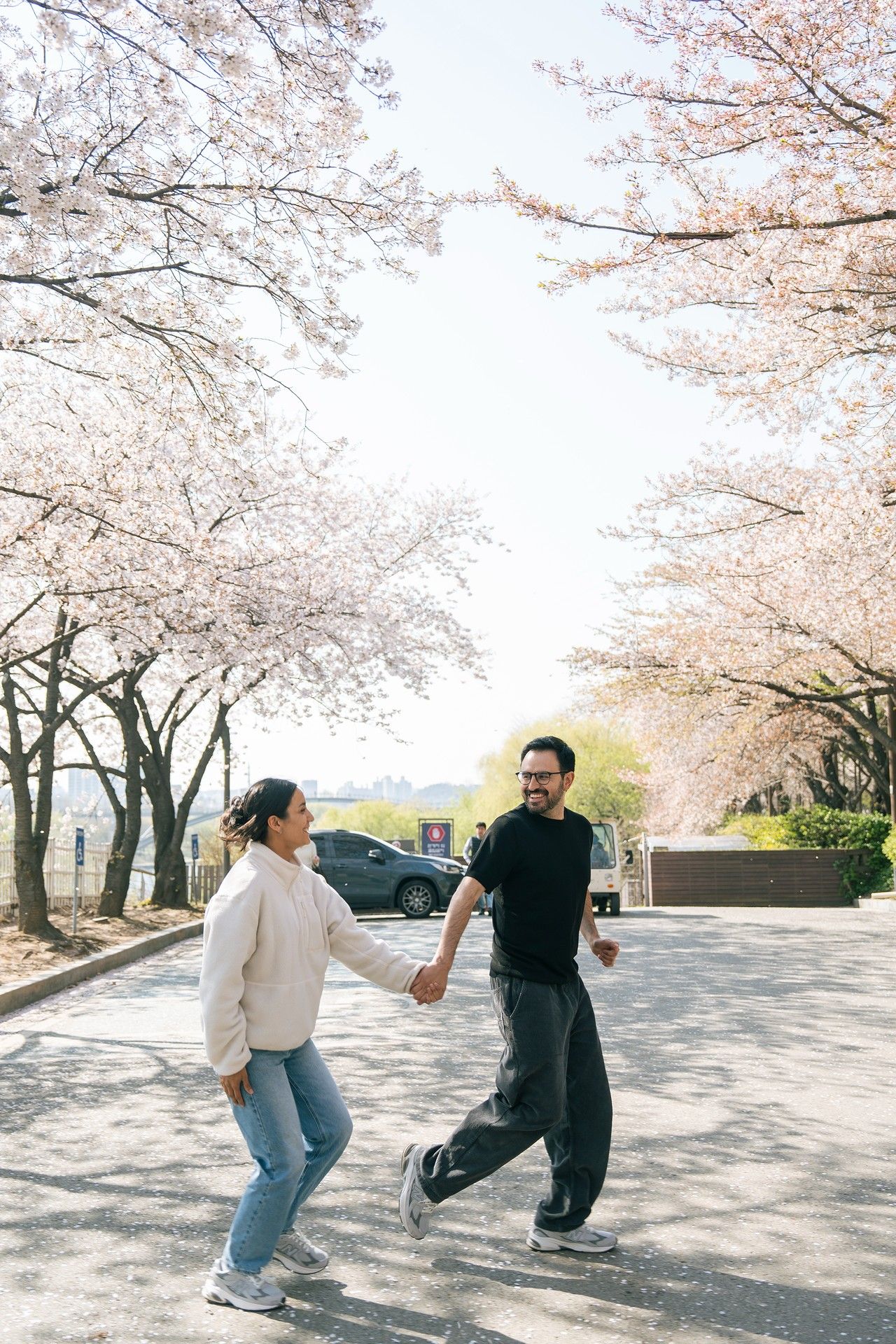 Couple holding hands and walking under blooming cherry blossom trees on a sunny spring day.