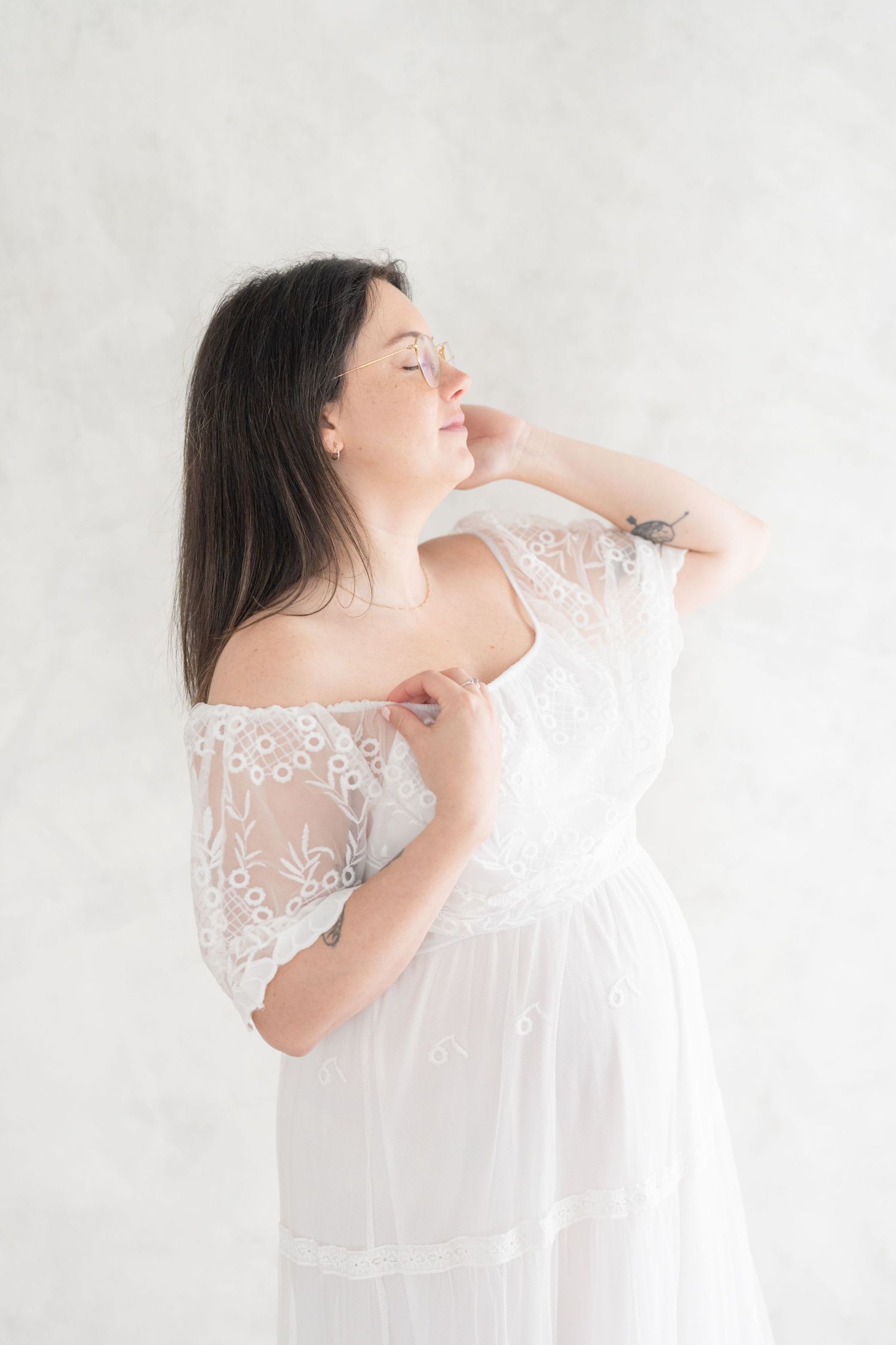 Portrait de grossesse fine art d'une future maman dans une robe de dentelle et tulle blanc vaporeux au studio privé de Saint-Augustin