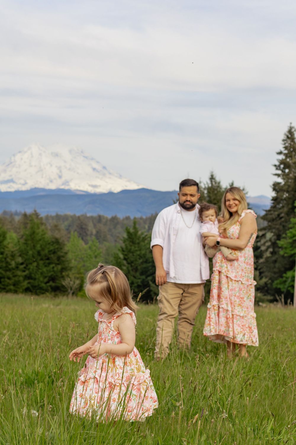 Family of four in floral and white outfits posing in green meadow with snow-capped Mount Rainier in background in eatonville washington