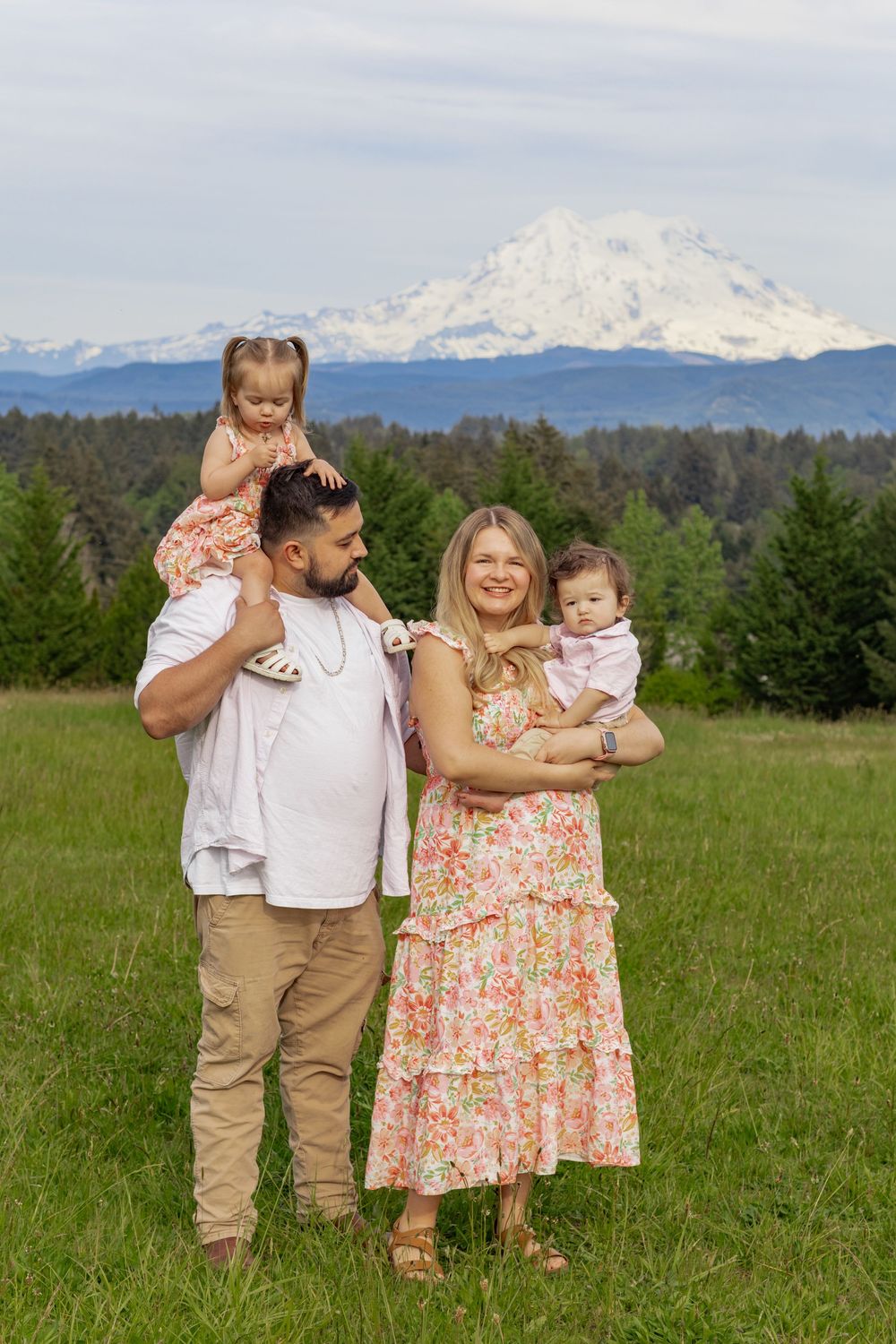 Family of four smiling in a green meadow, parents holding young kids with Mount Rainier behind them. taken by Washington state photographer
