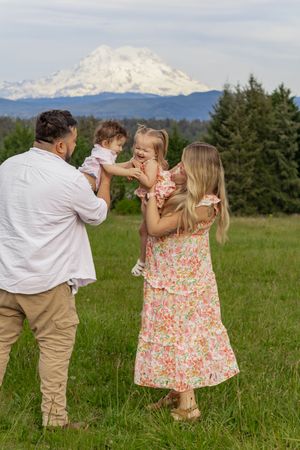 Parents in floral and white outfits playfully lifting two young kids in a meadow Mount Rainier behind, taken by pierce county photographer