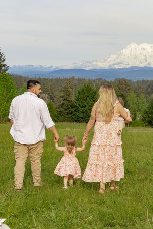 Family of four walking through green meadow holding hands with mount rainier in the back, taken by roy washington photographer
