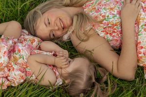 Mother and young daughter lying in green grass smiling and laughing together in matching floral dresses taken by washington photographer