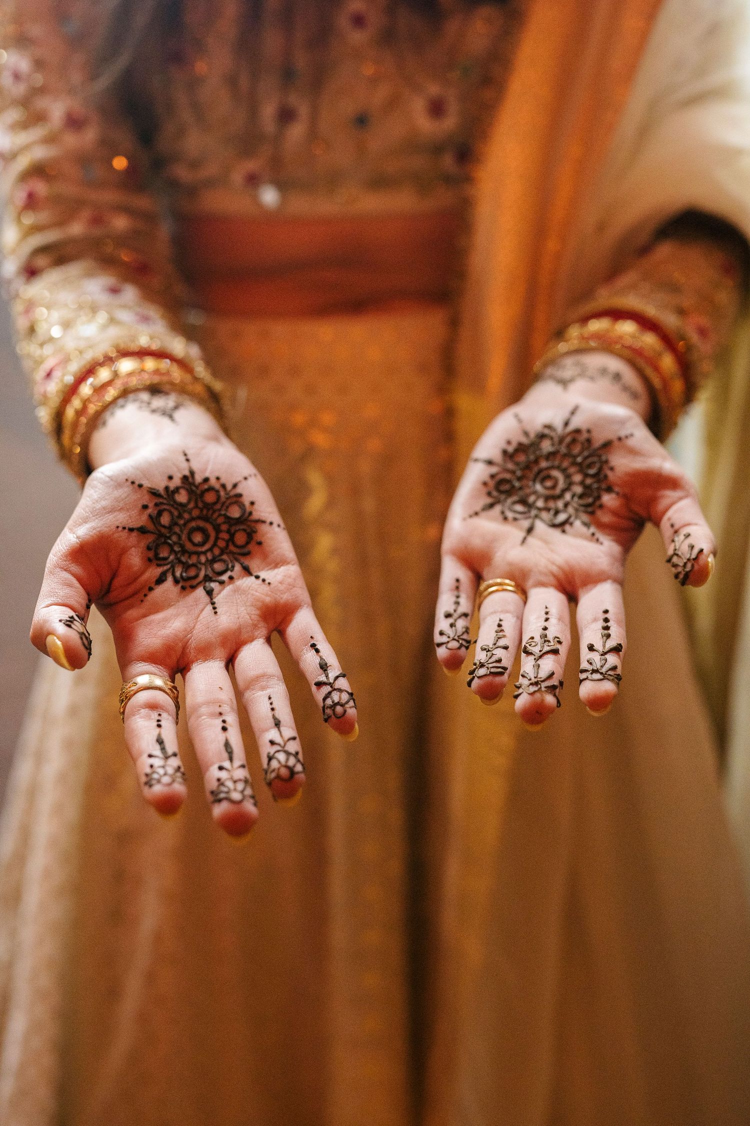 Indian couple in yellow outfits during Haldi ceremony, standing under stone arches with marigold flowers.