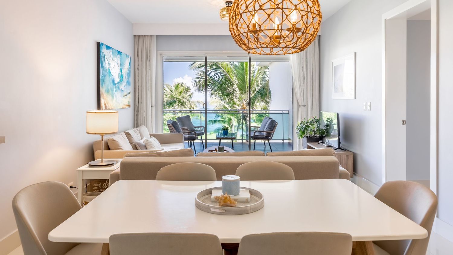 Contemporary dining room with rattan pendant light and window views of palm trees and ocean.
