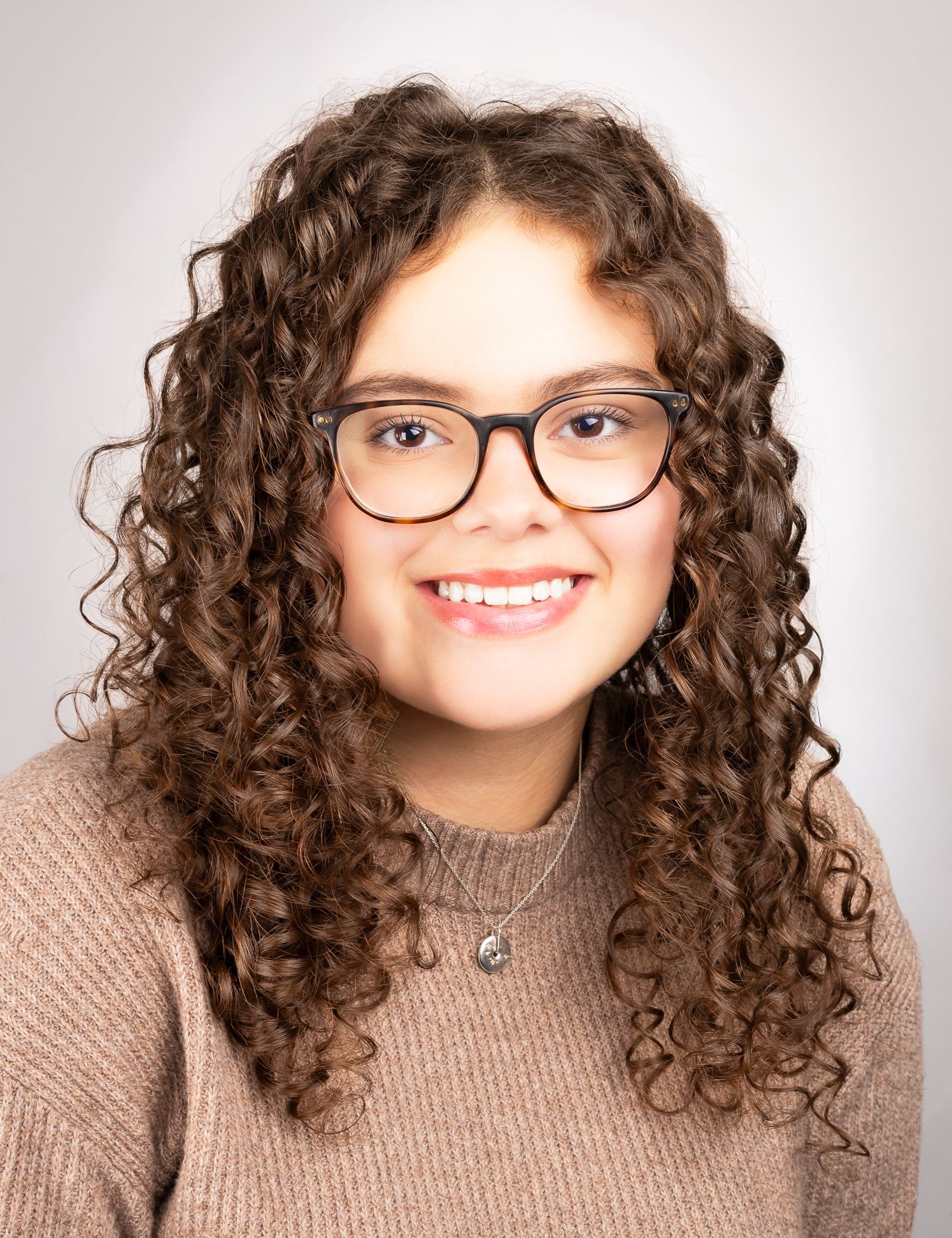 Image of a girl with glasses smiling at the camera, front shot, 2nd angle