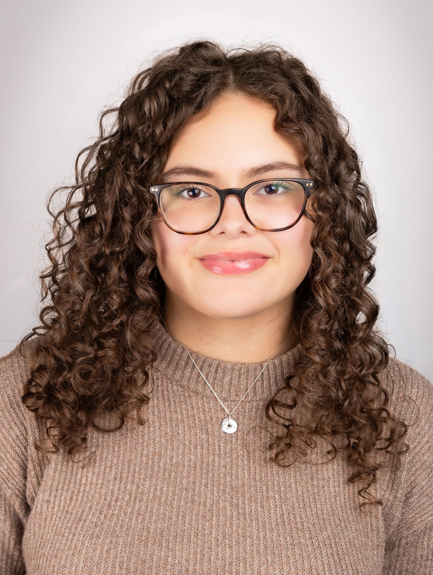 Image of a girl with glasses smiling at the camera with a closed mouth smile, front shot