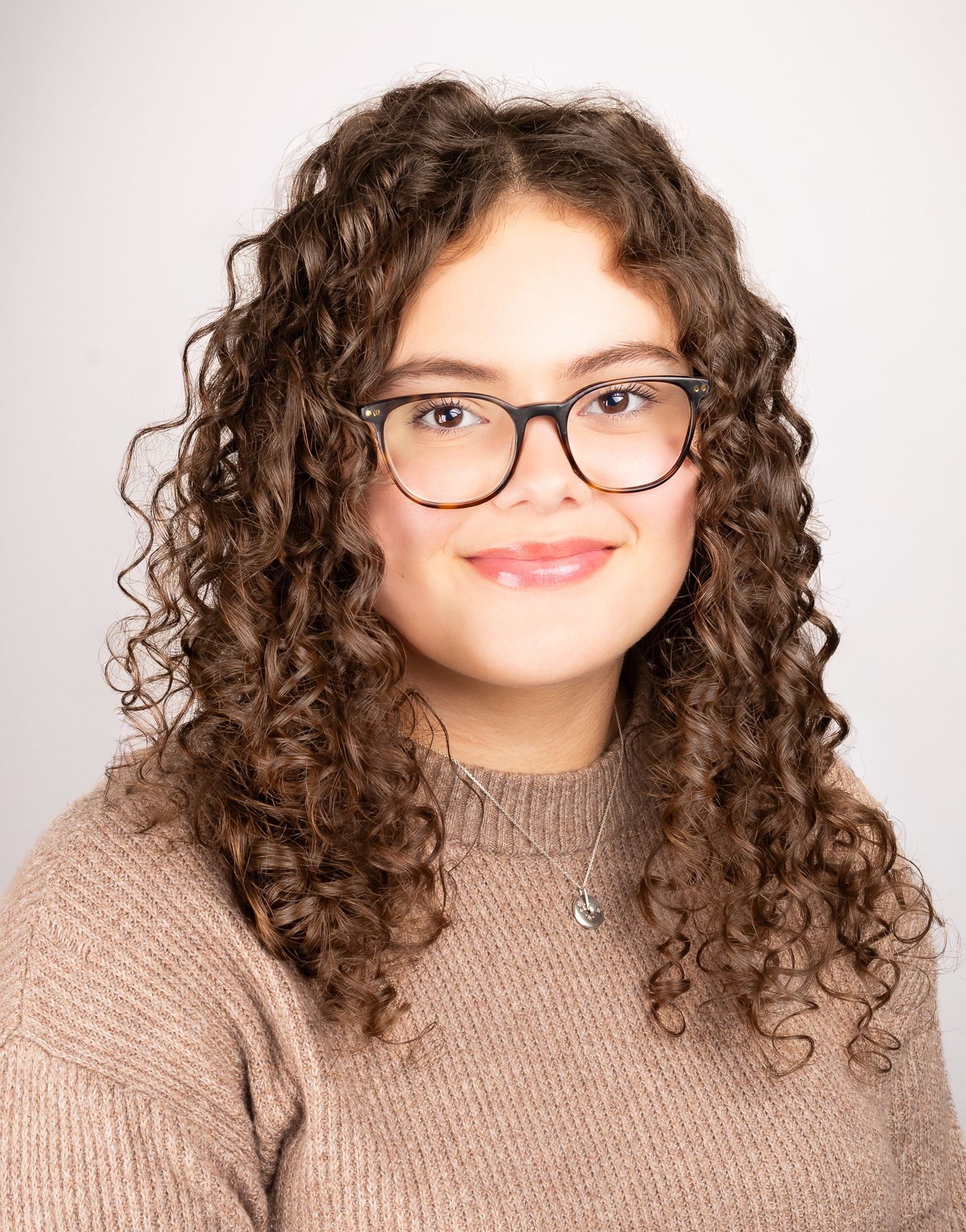 Image of a girl with glasses smiling at the camera with a closed mouth smile, front shot