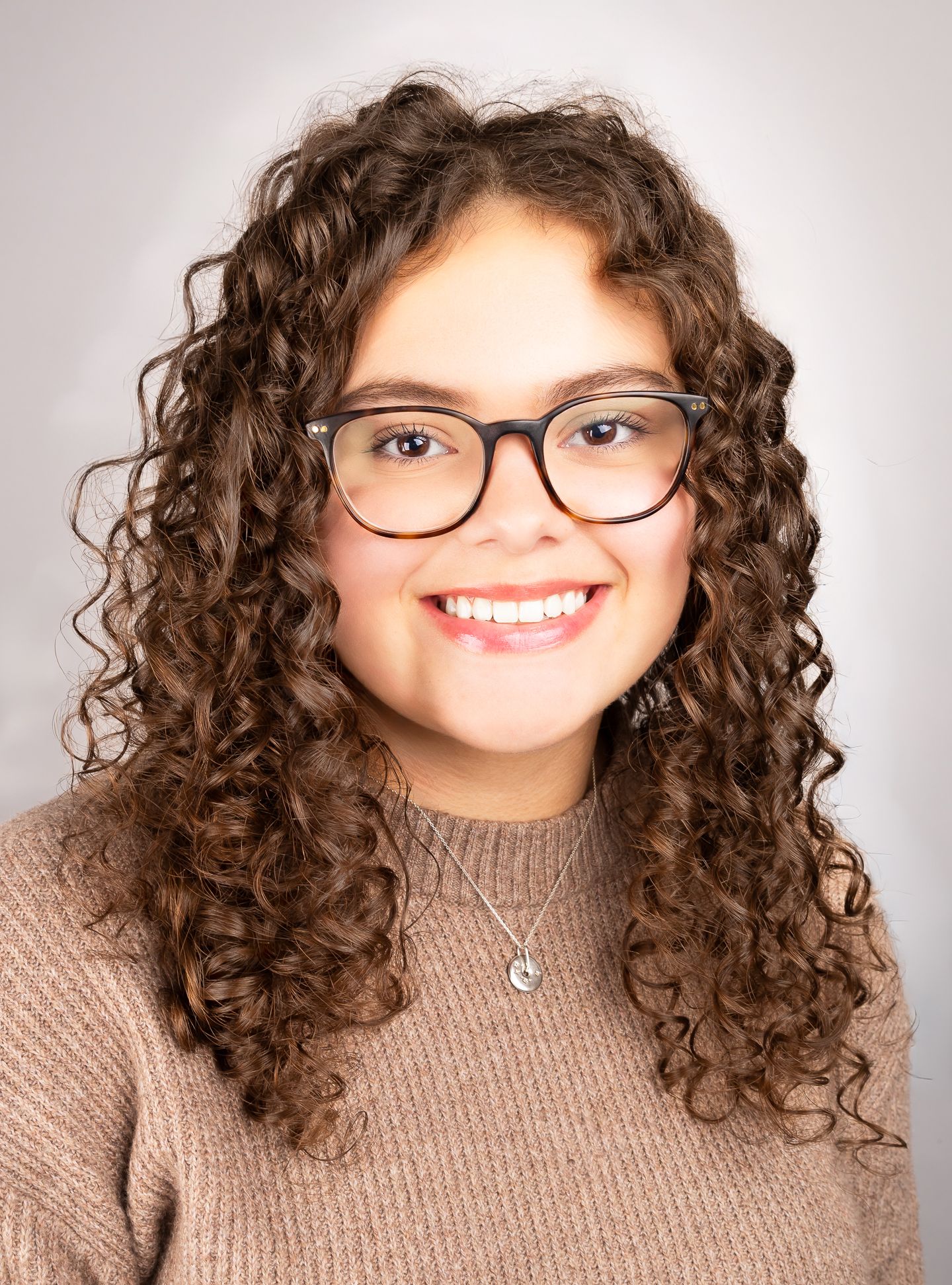 Image of a girl with glasses smiling at the camera with teeth, front shot