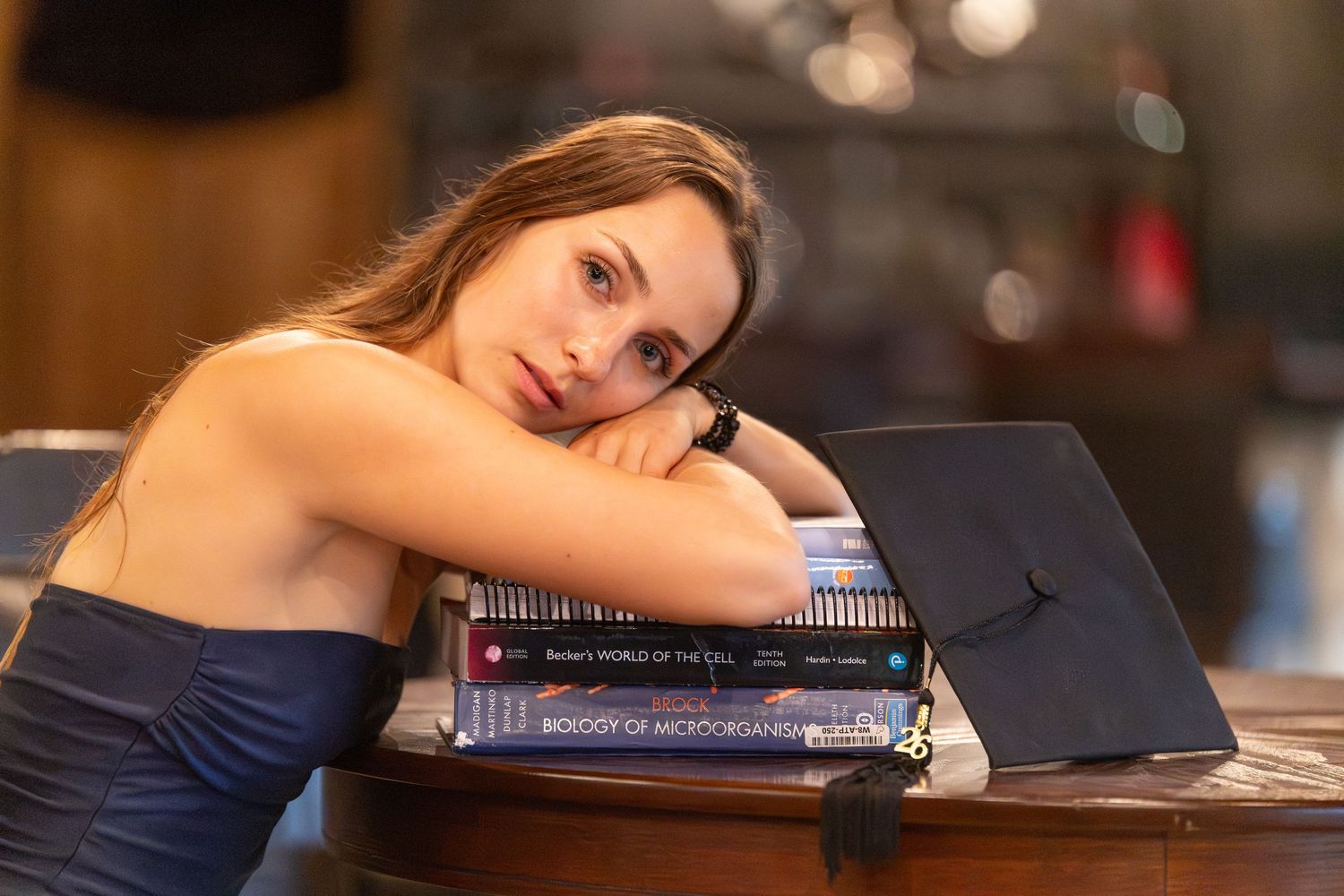 close up of girl resting her head on her study books with her graduation cap leaned against them
