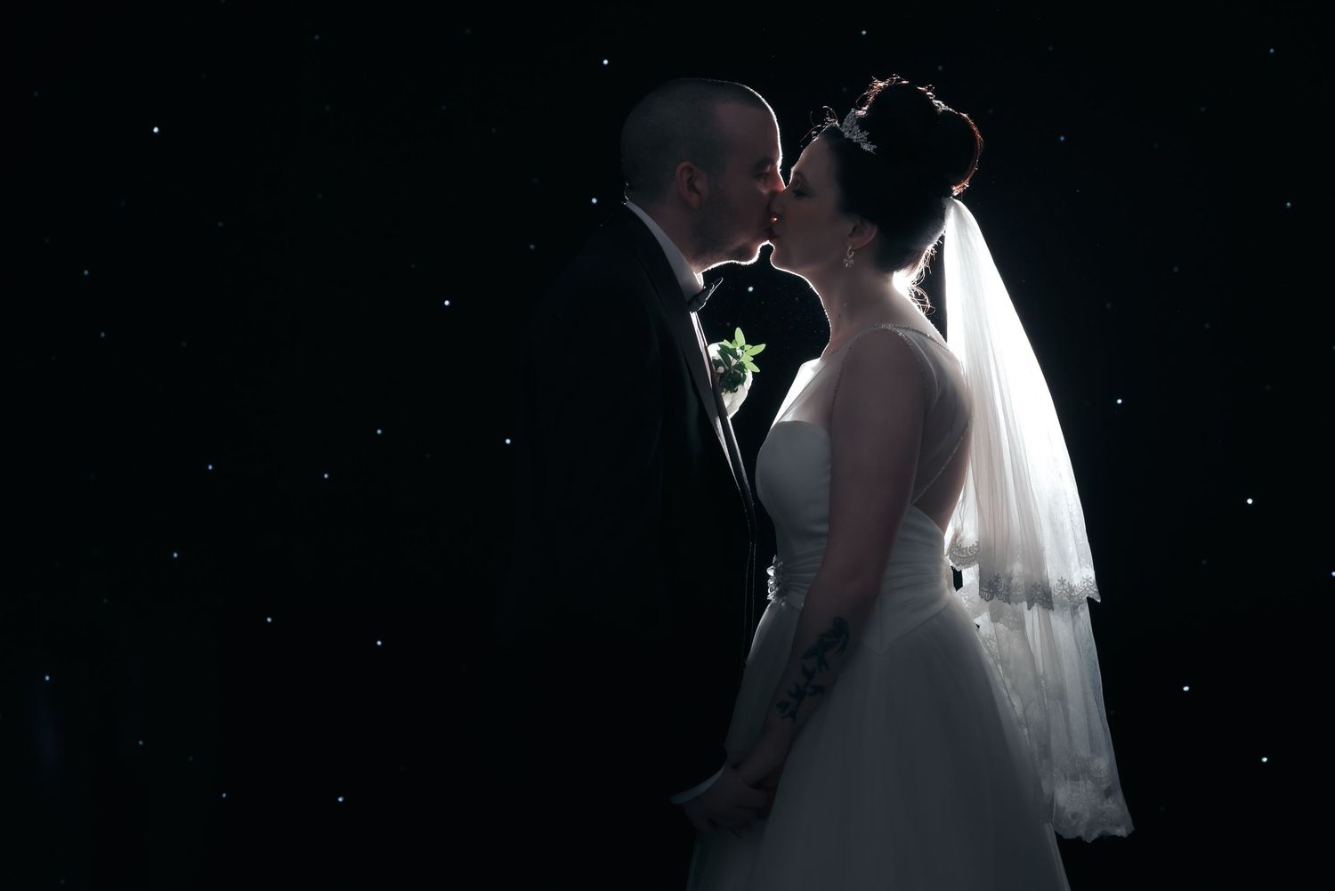 Bride and groom sharing a romantic kiss silhouetted against a dark starry background on their wedding day.