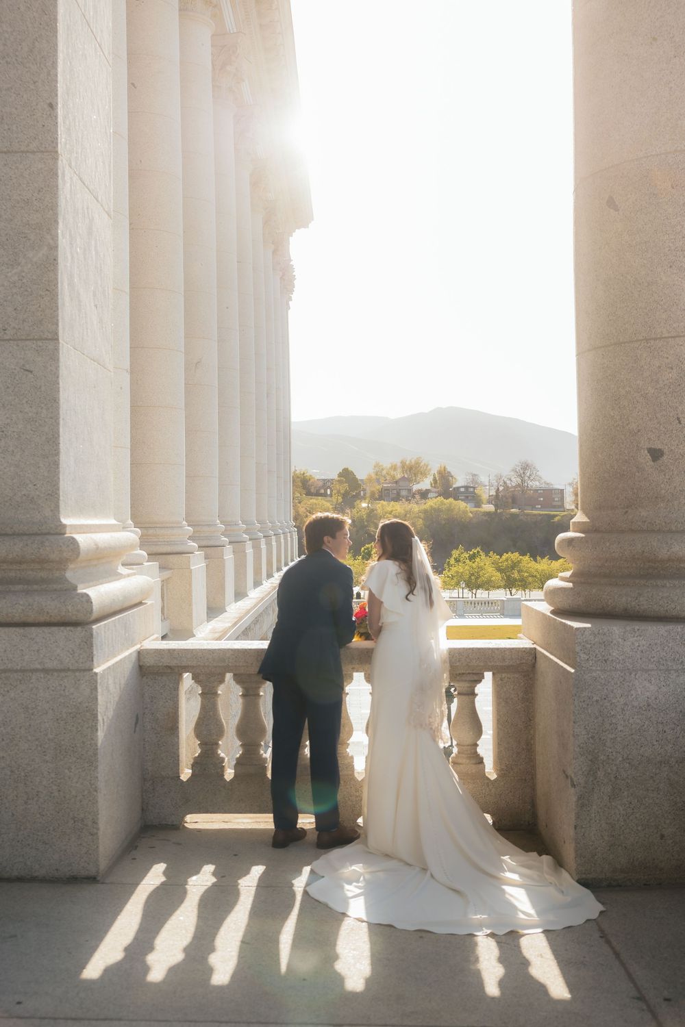 Bride and groom stand between grand columns at sunset, overlooking scenic mountain views on their wedding day.