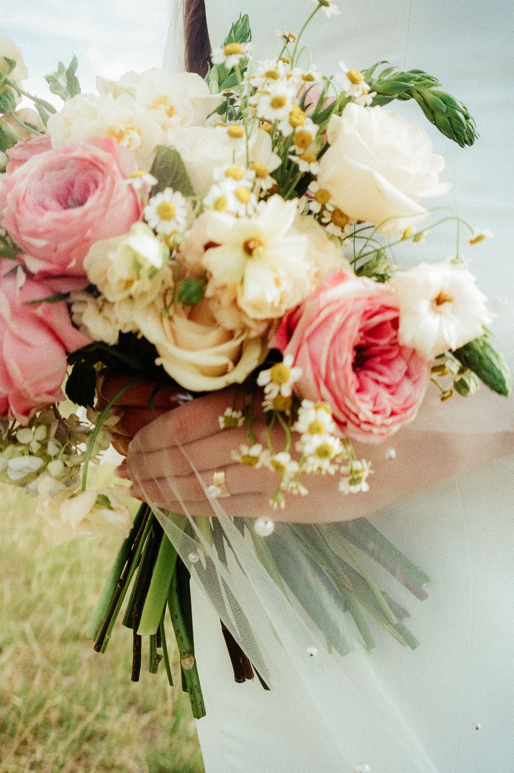 Close-up of bridal bouquet featuring pink garden roses, white peonies, and delicate wildflowers with veil.