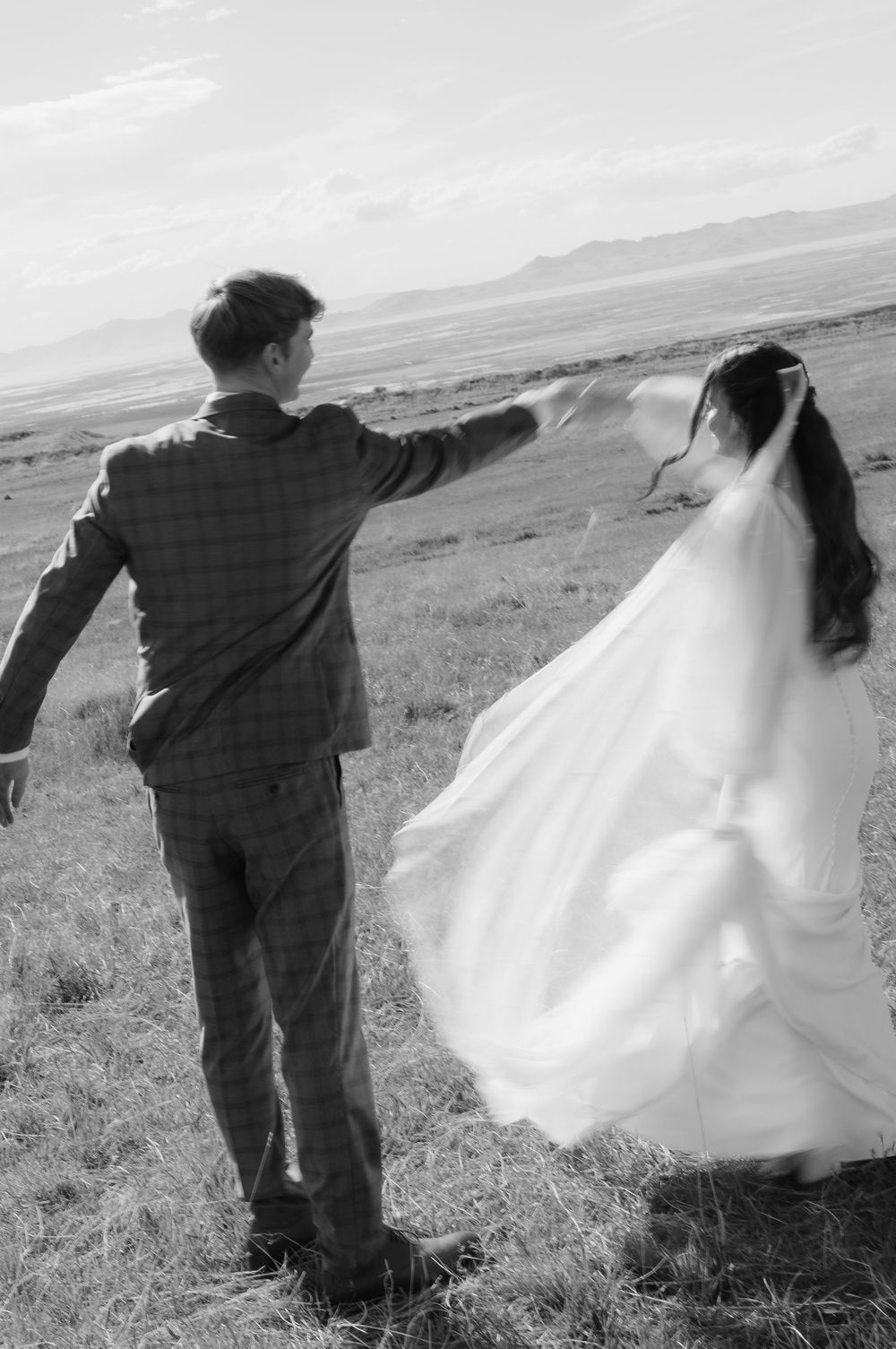 Black and white photo of bride and groom walking hand in hand across an open field.