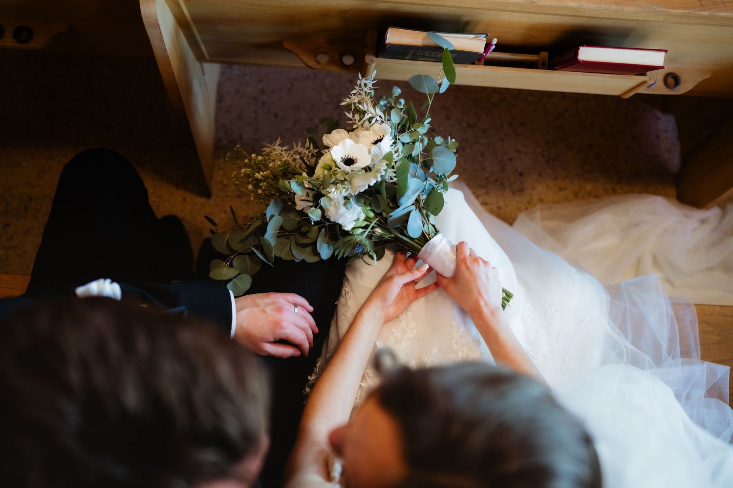 Bride and groom holding hands with a white floral bouquet on a wooden floor during wedding ceremony.