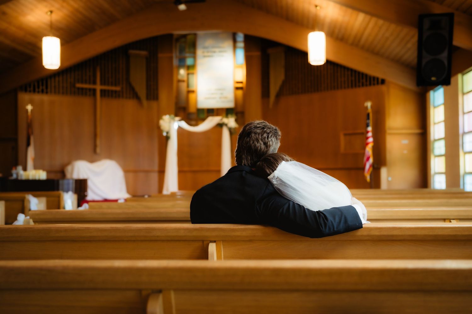 Couple sitting together on wooden church pew during wedding ceremony in a warmly lit chapel.