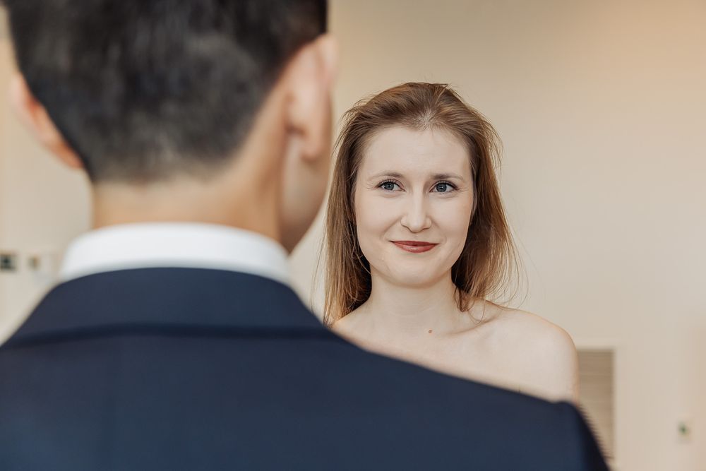 A bride gazes lovingly at her groom in a navy suit during a romantic wedding moment indoors.