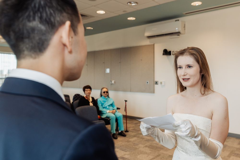 A bride in a white dress and gloves reads vows during an intimate courthouse wedding ceremony.