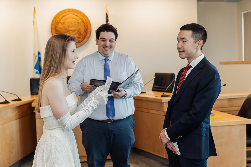 A smiling bride and groom stand with an officiant during a casual courthouse wedding ceremony.