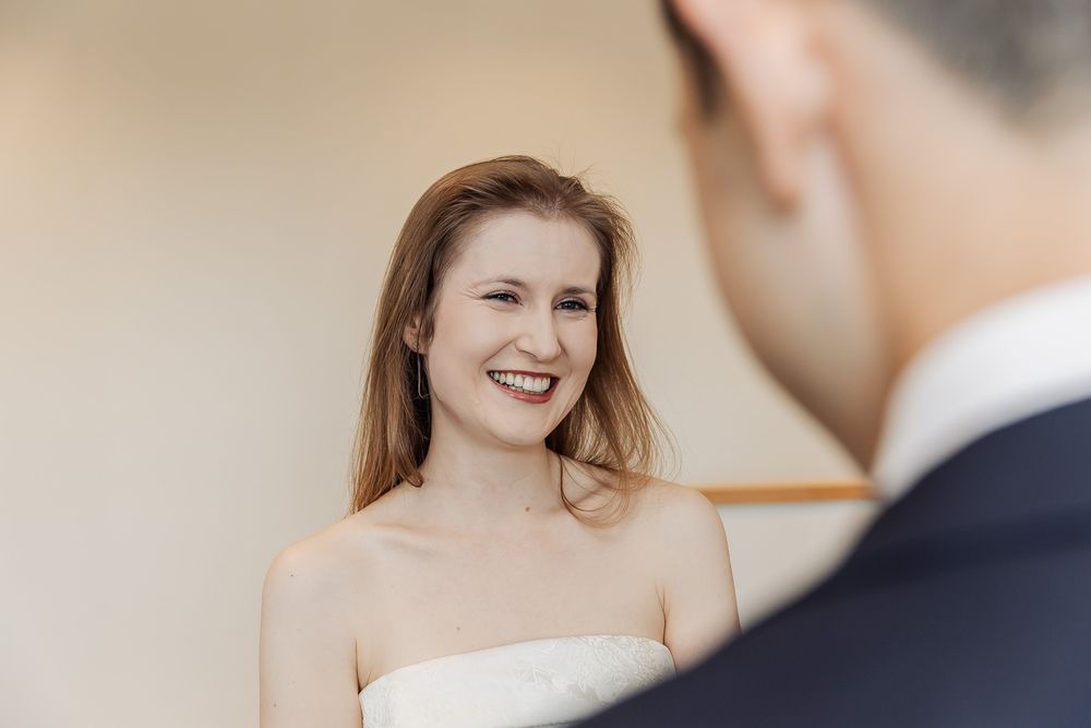 A happy bride in a white strapless dress smiles warmly at her partner during a wedding ceremony.