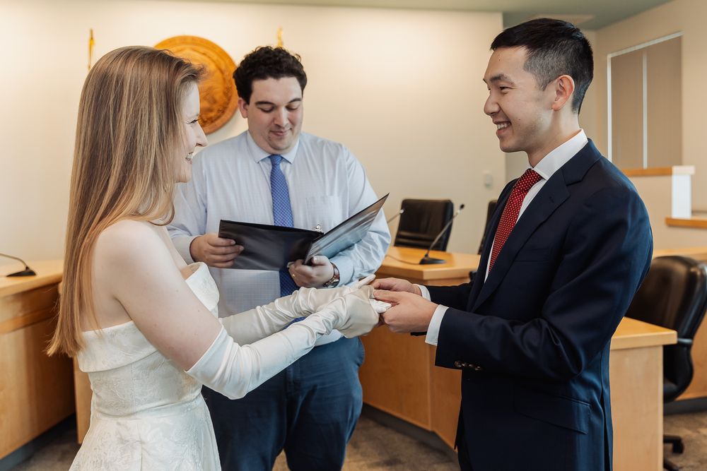 Couple exchanging rings during a civil wedding ceremony with an officiant holding a binder in an office.