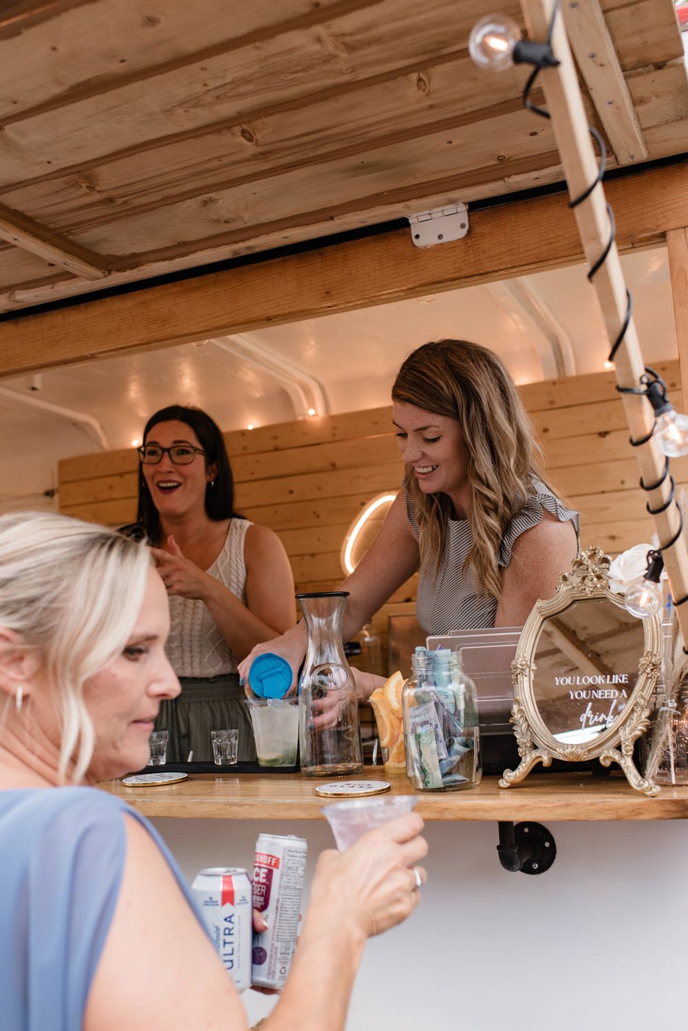 Three women laughing and socializing at a rustic wooden bar during an event.