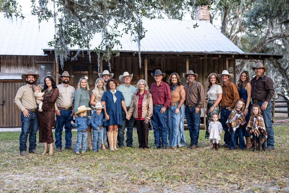 Large family group in cowboy hats posing together outside a rustic ranch building in a country western setting.