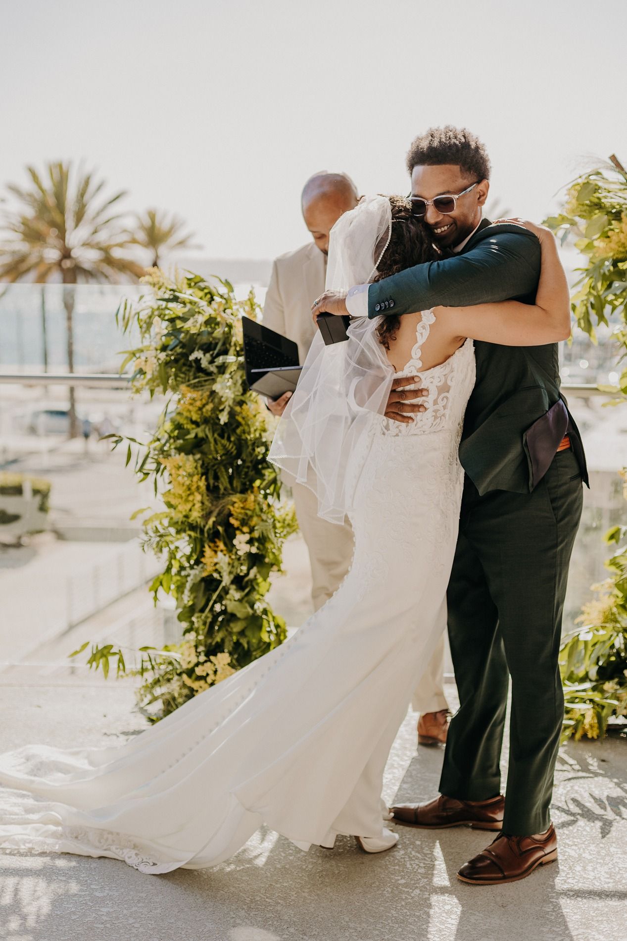 Bride and groom share a romantic embrace during outdoor wedding ceremony with lush greenery and palm trees at The Lane.