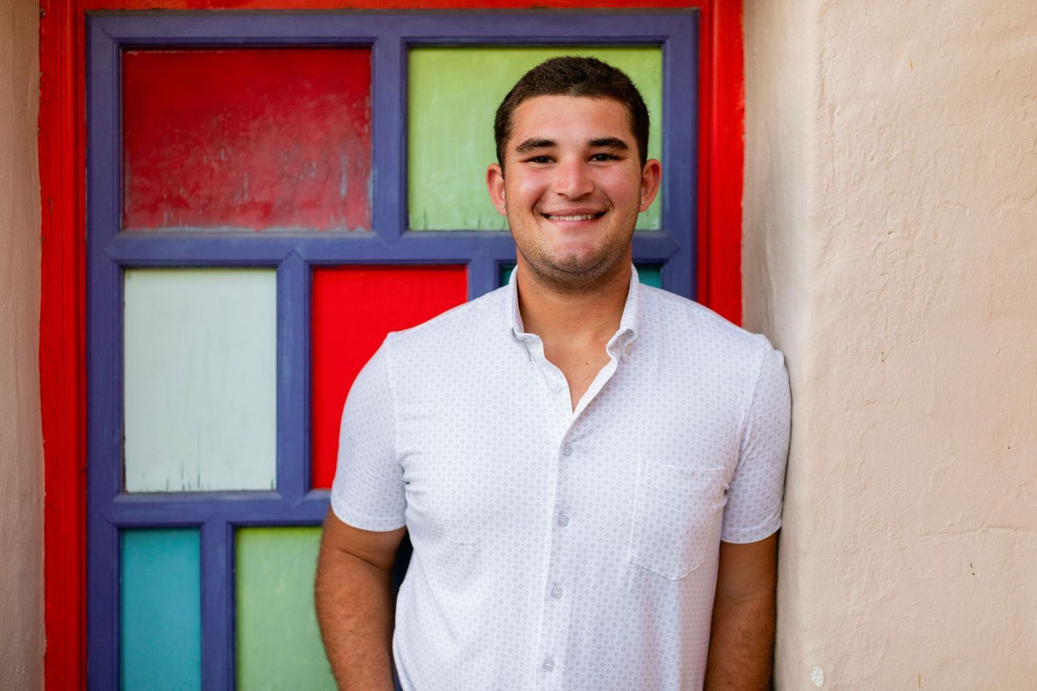 A high school senior standing in shadowy colonnade wearing casual blazer and jeans.