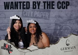 Two women wearing tiaras pose at Best of Charleston CCP wanted poster photo booth.
