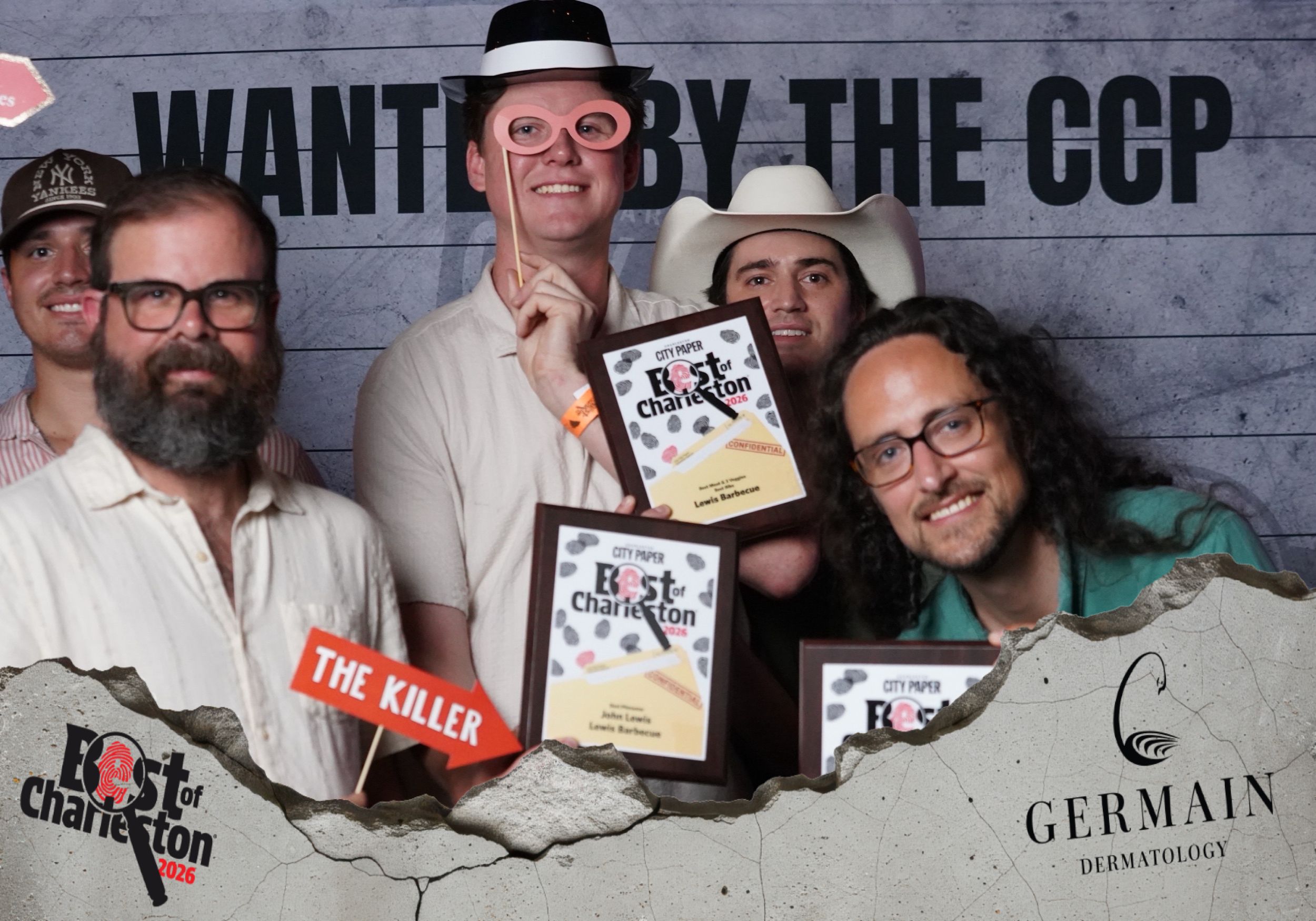 Group of five people posing at Best of Charleston awards event with plaques, wearing fun costumes, with CCP and Germain Dermatology banners.