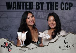 Two smiling women pose with champagne props at Best of Charleston CCP photo booth.