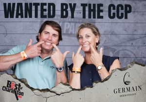 Smiling couple posing at a Best of Charleston CCP wanted photo booth backdrop at a party event.