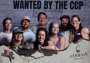 Group of seven smiling friends posing at a Best of Charleston event with Wanted by the CCP backdrop.