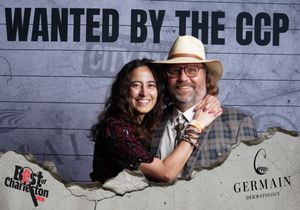 Couple smiling and embracing at Best of Charleston event with Wanted by the CCP themed photo backdrop.