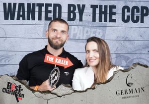 Man and woman posing at Wanted by the CCP photo booth, man holding The Killer prop sign.