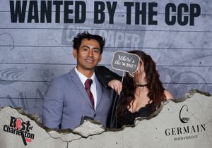 Couple posing playfully at Best of Charleston event with Wanted by the CCP photo backdrop.