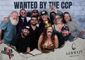 Large group with fun props poses at Best of Charleston Wanted by the CCP themed photo booth.