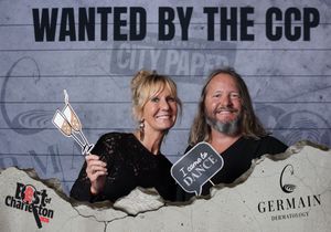 Couple posing at Best of Charleston CCP wanted photo booth, woman holding award trophy prop.