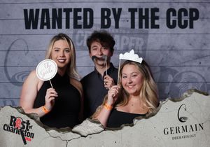Three friends smile at Best of Charleston CCP wanted poster photo booth with fun props.