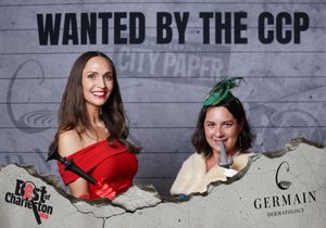 Two women smile at a Best of Charleston event featuring a Wanted by the CCP themed photo backdrop.
