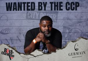 Man posing under a 'Wanted by the CCP' sign at a City Paper Best of Charleston event sponsored by Germain Dermatology.