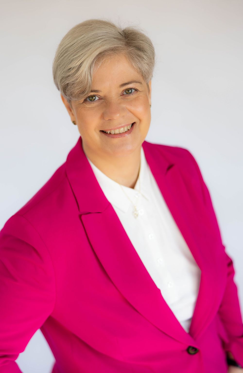 Professional woman in bright pink blazer and white blouse smiling confidently against a light background.