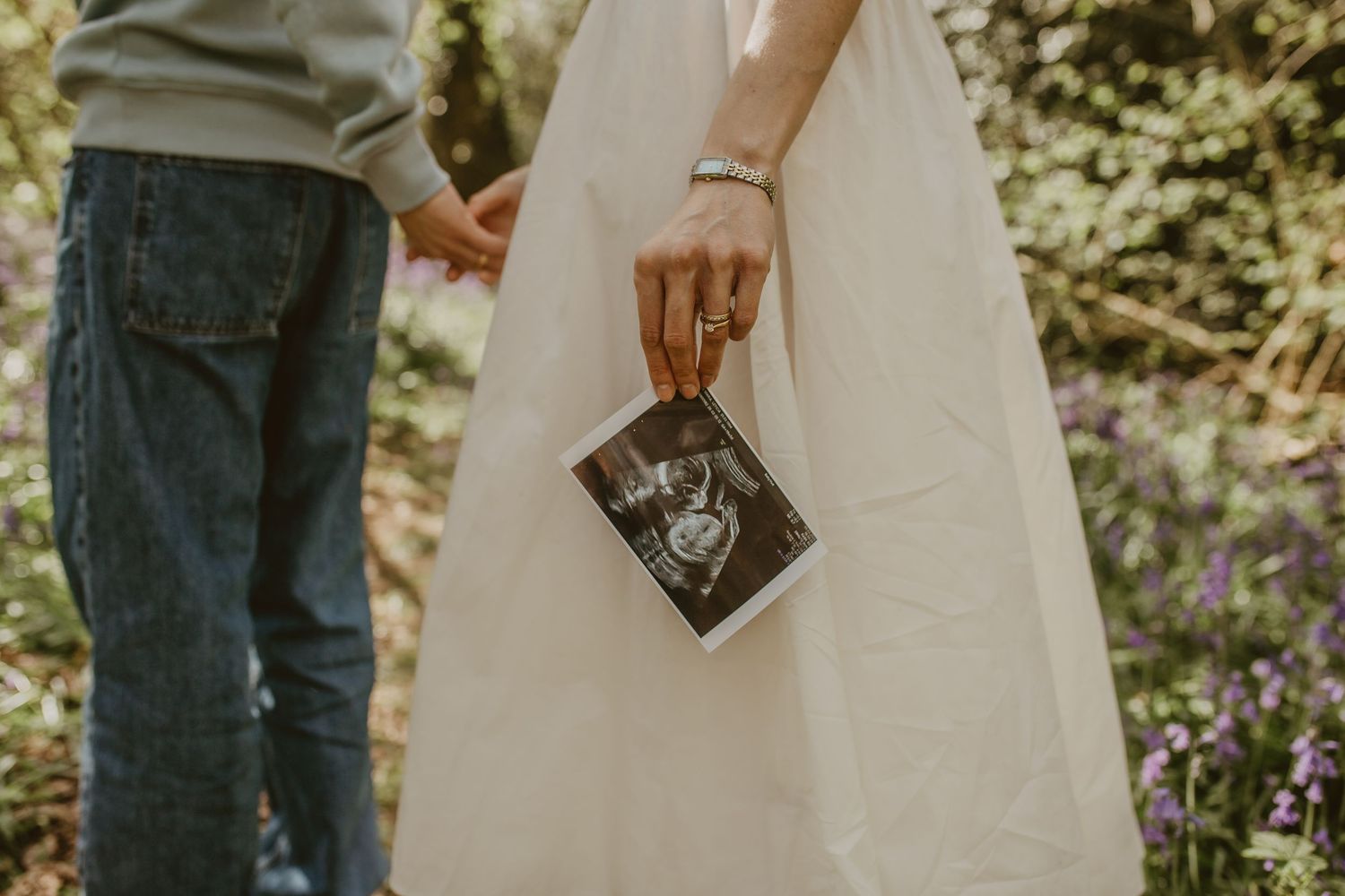 Couple holding hands outdoors displaying a baby ultrasound photo, pregnancy announcement in a garden setting.